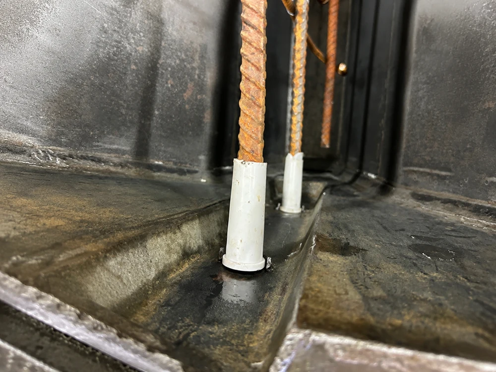 Rusty rebar rods with white plastic sleeves in metal base