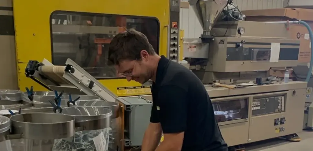 Jeune manœuvre emballant des sacs de pièces fabriquées par Plasti-Tom à l'intérieur de l'usine.