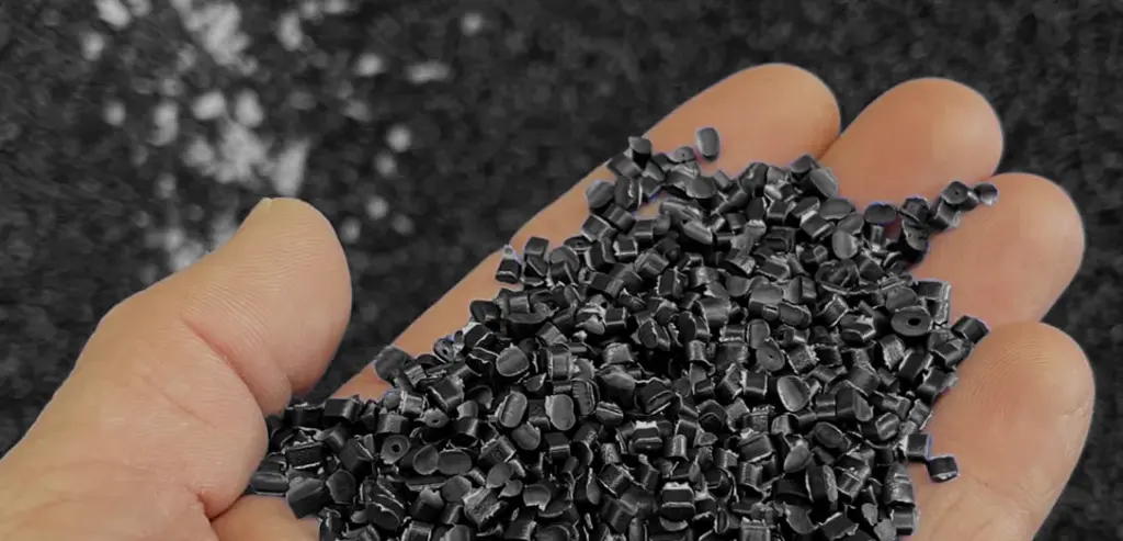 hero procede de moulage plasti tom Main avec une poigné de granules de plastique noir Plasti-Tom.